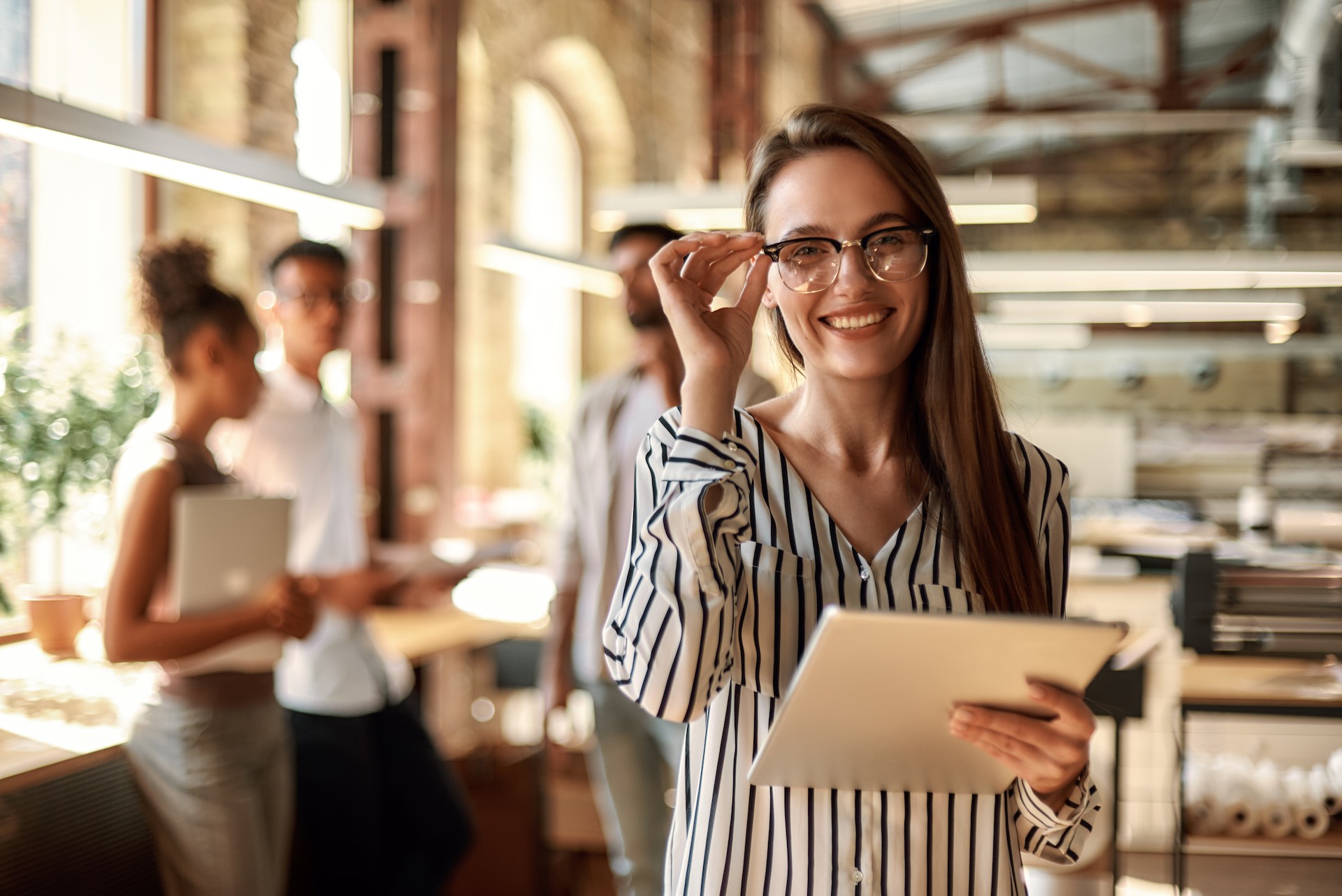 Successful business woman. Young cheerful woman holding digital tablet and looking at camera with smile while standing in the modern office. Business concept. Job