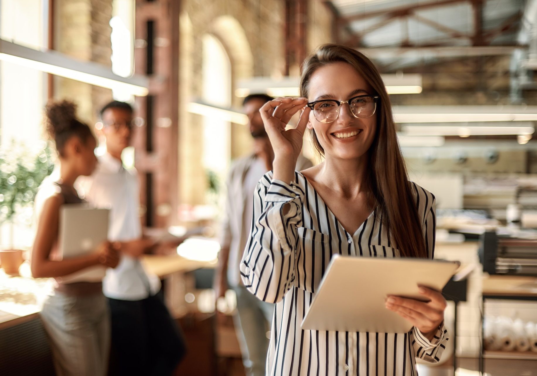 Successful business woman. Young cheerful woman holding digital tablet and looking at camera with smile while standing in the modern office. Business concept. Job