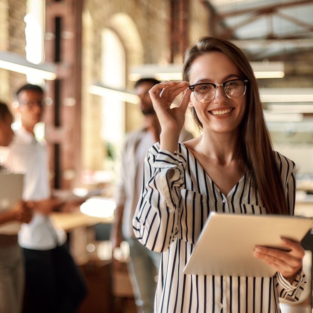 Successful business woman. Young cheerful woman holding digital tablet and looking at camera with smile while standing in the modern office. Business concept. Job